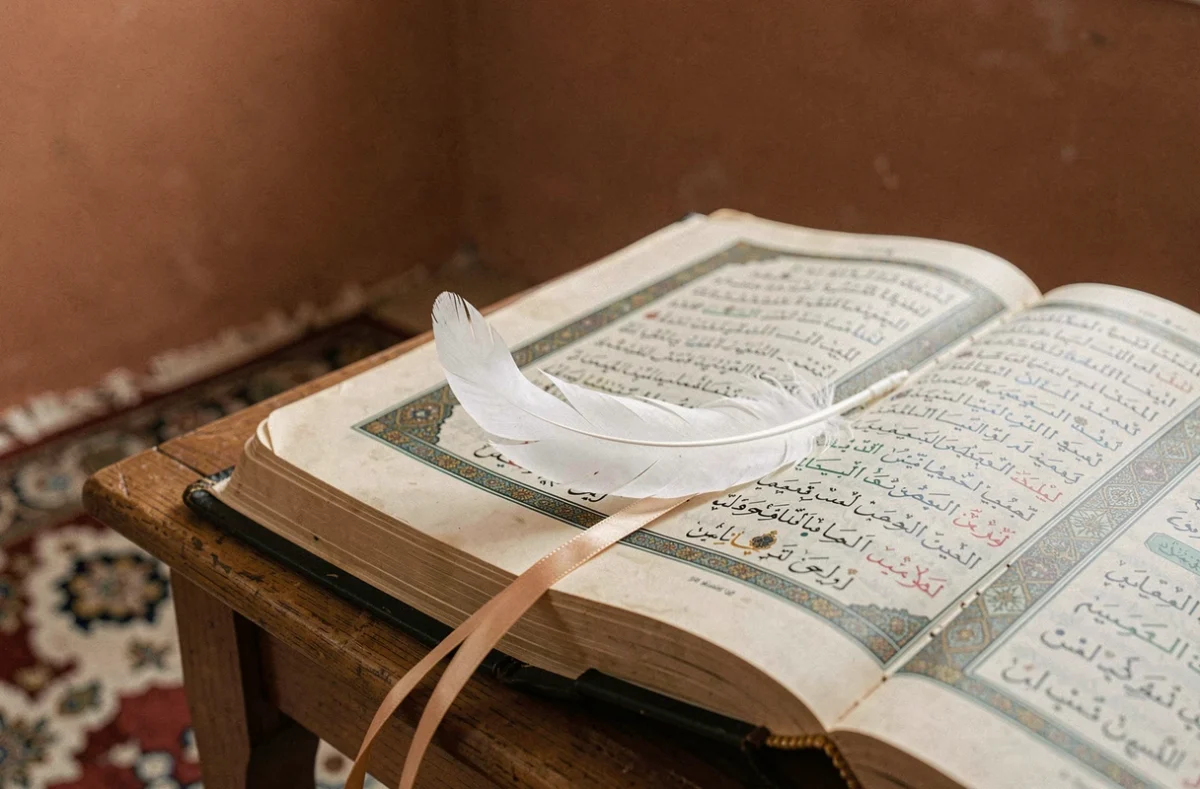 Une plume blanche posée sur un Coran ouvert, symbole spirituel en islam